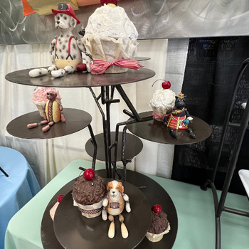 A tiered metal stand displays whimsical dog figurines creatively made from cupcakes and sweets. Each dog is accessorized, creating a playful atmosphere.