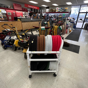 A hardware store interior with various colored coiled ropes on a white cart. Lawn equipment lines the wall, and customer service is in the background.
