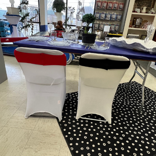 Two white chairs with red and black sashes face a table set with elegant glassware and a purple tablecloth. The setting is warm and inviting.