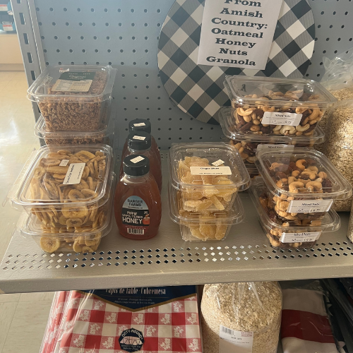Containers of mixed nuts, dried fruit, granola, and honey bottles are displayed on a shelf with a sign reading 