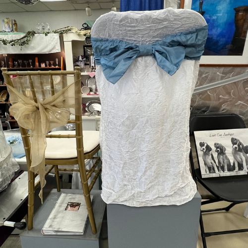 Two chairs covered in decorative fabric are displayed. One has a gold cover with a bow, the other a white cover with a blue bow. A poster of penguins is nearby.