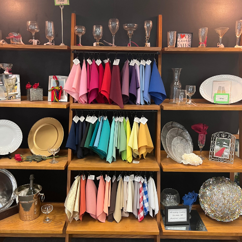 A display of colorful napkins in various shades hangs on shelves alongside elegant glassware and decor. The setting conveys a stylish, celebratory tone.