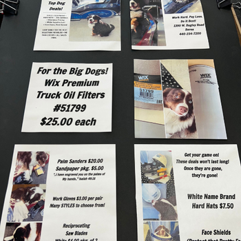 Flyers on a table advertising various products and deals, including oil filters, sanders, and hard hats, with images of dogs and tools. The tone is lively and promotional.