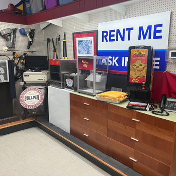 Shop interior with rental items on display. Tools, a popcorn machine, and a nacho cheese dispenser are on a countertop. A "Rent Me" sign is visible.