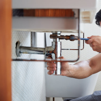DIYA plumber fixing a sink pipe uses a tool under a bathroom sink. The image focuses on the hands and plumbing, conveying focus and professionalism.